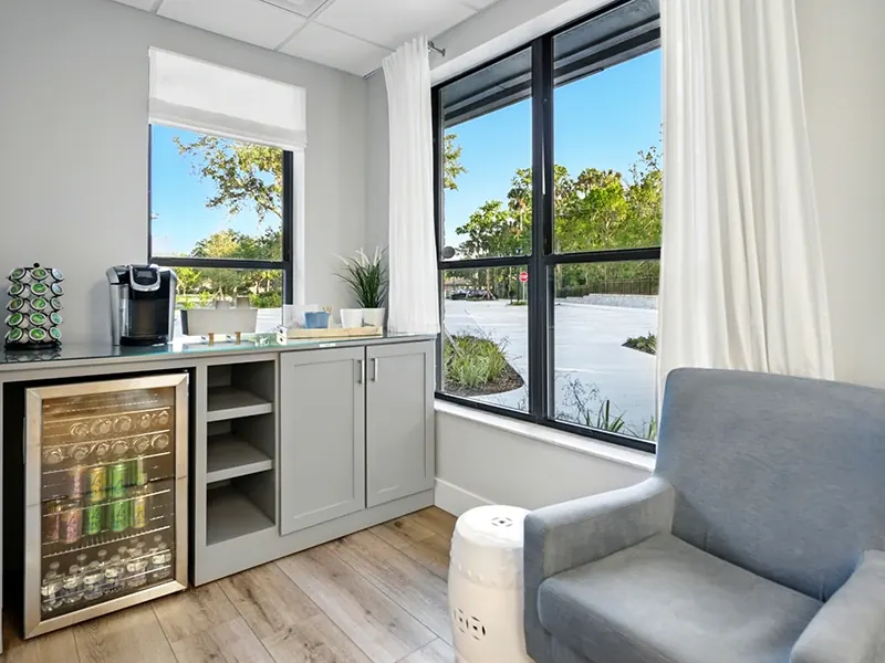 The coffee station and drinks fridge beside an armchair and window.